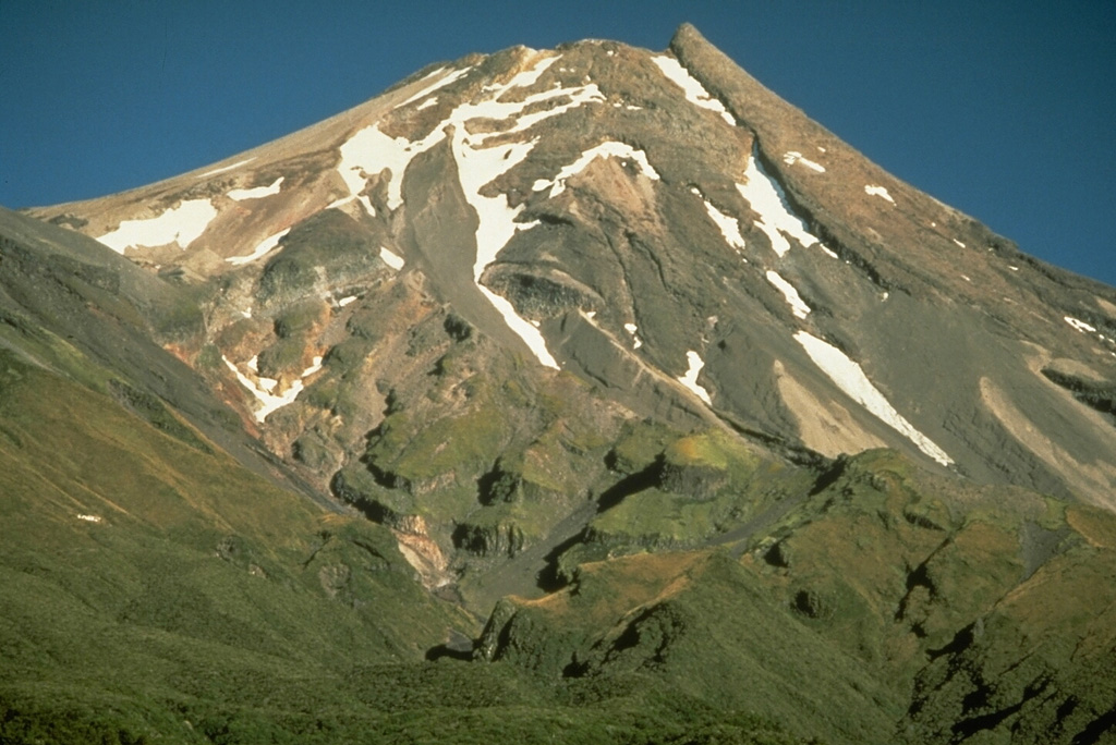Taranaki volcano (previously called Egmont) has a breached summit crater that is occupied by a partially-destroyed lava plug. This view from the SE shows the stacked lava flows that form much of the cone, with the vegetated slopes of the parasitic cone, Fanthams Peak, at the left.  Photo by Chris Newhall, 1986(U.S. Geological Survey).