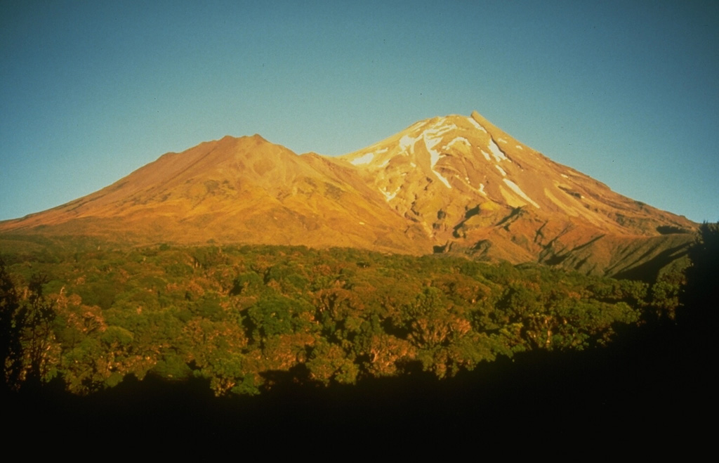 Taranaki, seen here from the SW, rises above the Taranaki ring plain, with Fanthams Peak on the left. It is the youngest and SE-most of a group of volcanoes beginning with the Kaitoke Range, near the W coast of North Island. Its most recent activity, during the 15th to 19th centuries, included the eruption of ash plumes, pyroclastic flows that traveled to the NW, and emplacement of the summit lava dome. Photo by Chris Newhall, 1986 (U.S. Geological Survey).