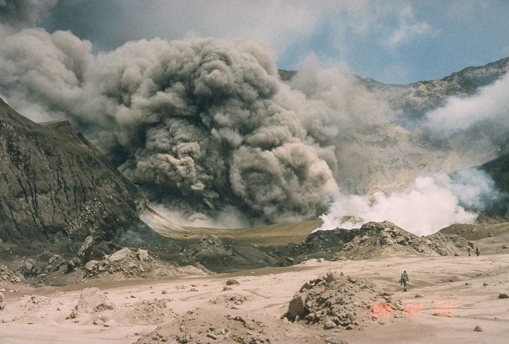 A New Zealand Geological Survey volcanologist on the crater floor of White Island (also called Whakaari) volcano observes an ash plume on 9 February 1989. This was one of many small-to-moderate explosive eruptions that took place between 1986 and 1994. Photo by Ian Nairn, 1989 (Geological Survey of New Zealand).