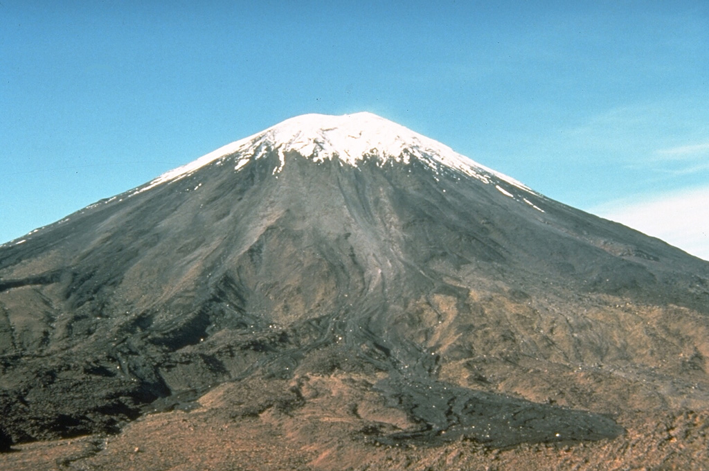Snow-capped Ngauruhoe volcano rises above the Mangatepopo track on the NW side of the volcano. The dark lobe in the right foreground is a deposit produced by lithic-rich pyroclastic flows during the 1975 eruption. Meter-scale ballistic blocks from powerful Vulcanian explosions during the 1975 eruption were ejected out to distances of 2.8 km, beyond the location of this photo. Photo by Don Swanson, 1984 (U.S. Geological Survey).