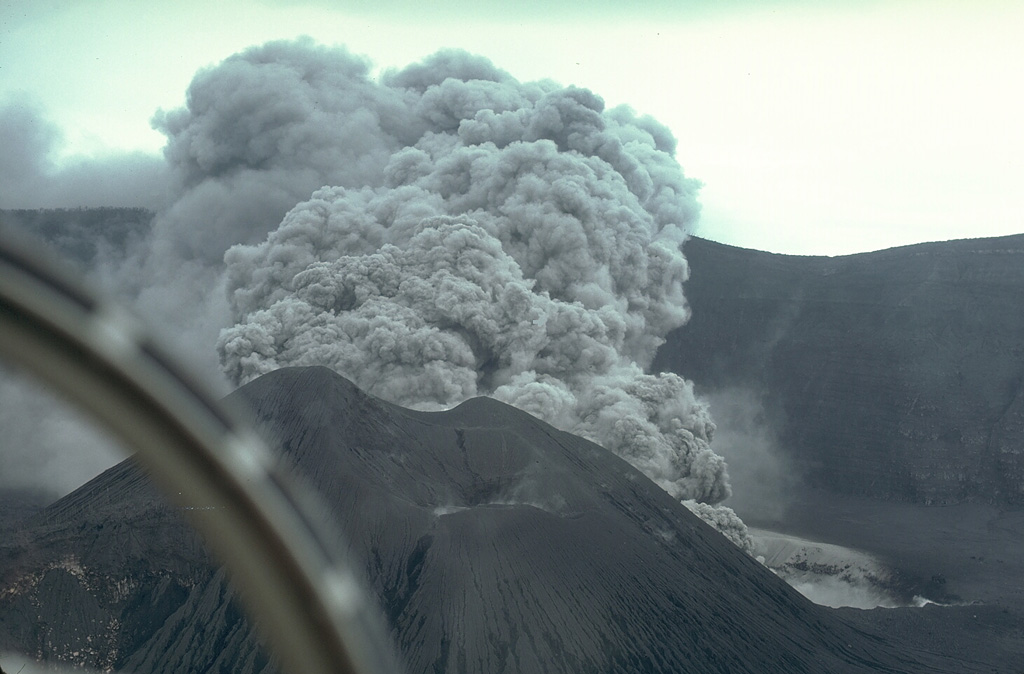An ash plume rises above a new vent behind Bagiai cone on the floor of Karkar's summit caldera on 17 April 1979. Phreatic eruptions had begun during the night of 12-13 January after six months of increasing seismicity and incandescence. Major phreatic explosions from the new vent on 8 March devastated the caldera rim area, killing two volcanologists who were monitoring the eruption. A new crater formed and intermittent moderate-to-strong explosive activity continued until 9 August. Photo by William Melson, 1979 (Smithsonian Institution)