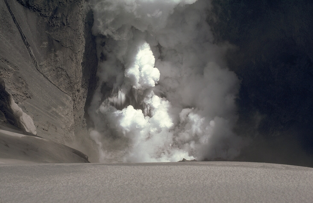 An ash plume from a phreatic explosion rises above a small crater lake at Karkar volcano on 22 April 1979. Following a major explosion from a new vent on the floor of the caldera on 8 March, minor explosions took place until May, after which activity intensified. A lake was briefly seen the day after this photo was taken. The lake disappeared after a strong explosion that night, which deposited ash on the SW caldera floor. Photo by William Melson, 1979 (Smithsonian Institution)