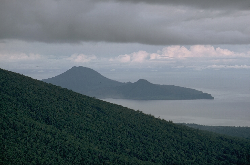 Lolobau is located on the western rim of a 6-km-wide caldera, which formed about 12,000 years ago on the 8 x 13 km Lolobau Island. It is seen here from the south beyond the lower flanks of Ulawun. The smaller peak to the right is located along the eastern caldera rim. Photo by Robert Citron, 1970 (Smithsonian Institution; courtesy of William Melson)