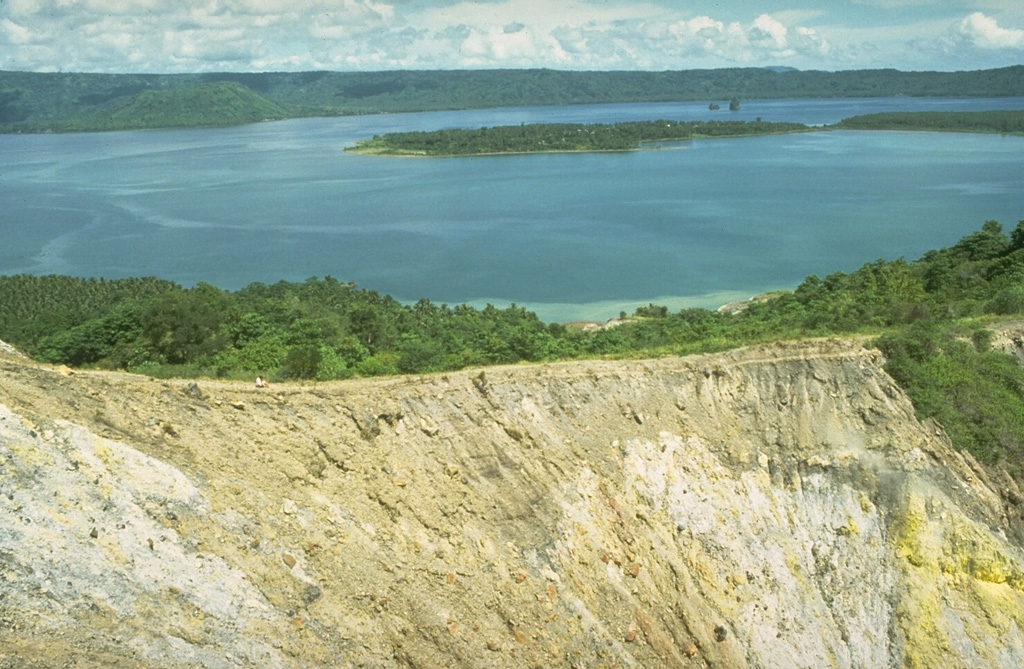 Rabaul caldera is seen here in 1984 beyond the sulfur-coated walls of Tavurvur crater, located on a post-caldera cone on the NE side of the caldera. Matupit Island lies across Greet Harbor, and the flat-topped Vulcan cone appears on the opposite side of the caldera below the low western caldera rim. Photo by Dan Dzurisin, 1984 (U.S. Geological Survey).