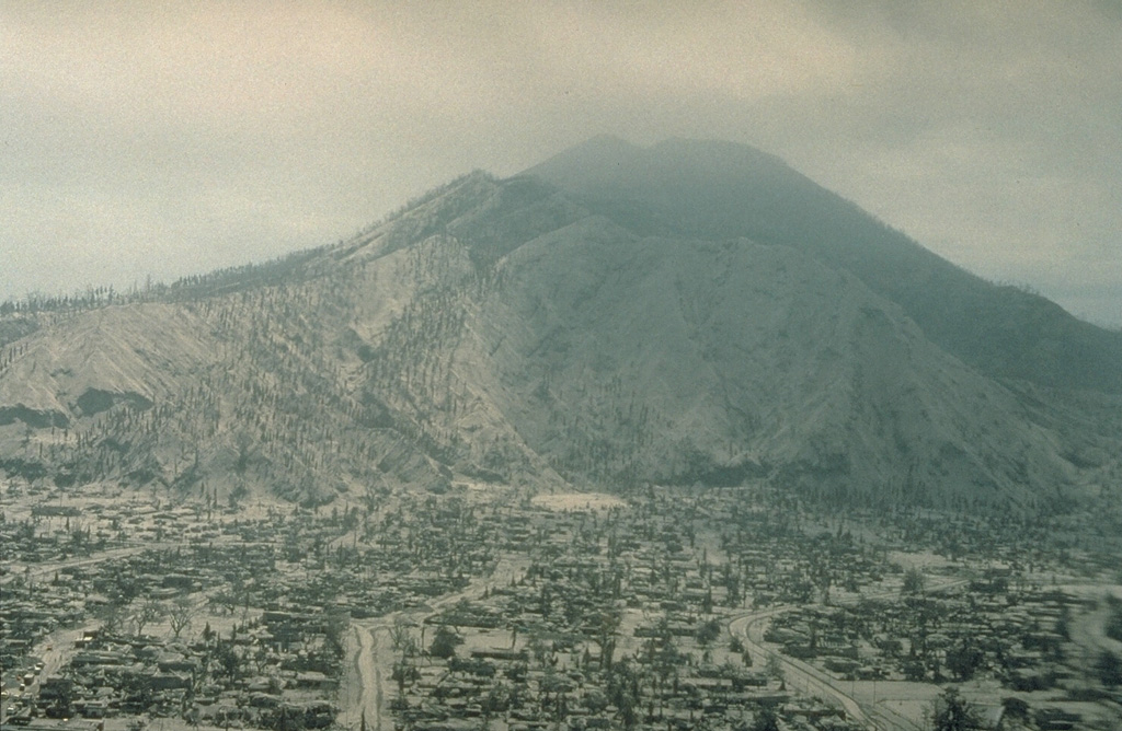 The city of Rabaul lies buried beneath a thick blanket of ash from the 1994 eruption. Mount Kombiu rises to the west above the deserted streets of the town. Ashfall from Tavurvur volcano during the first few days of the eruption caused widespread damage. Virtually every building in the south part of the town collapsed. Heavy rainfall at the time of the eruption produced lahars that caused additional damage. Photo by Andy Lockhart, 1994 (U.S. Geological Survey).