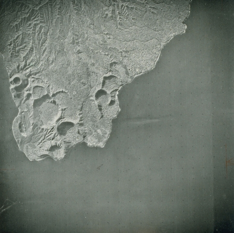 A series of basaltic tuff rings and a scoria cone occupy the western tip of Ambrym, at the subaerial end of a fissure system that cuts across the length of the island. The largest tuff ring is about 1 km in diameter. The tuff rings were produced by phreatic eruptions when magma interacted with the water table or near-surface, water-saturated sediments along the coast. At higher elevations along the rift zone, scoria cones predominate. Photo by Hunting Surveys, London (published in Green and Short, 1971).