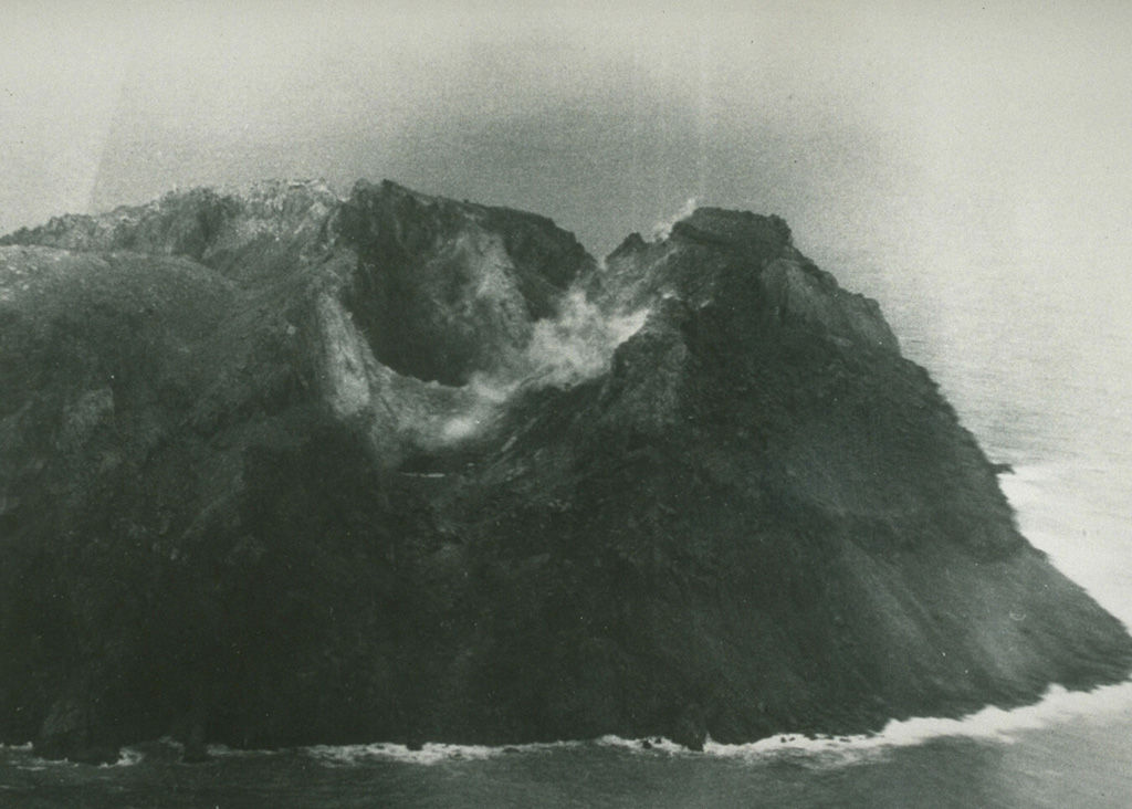 Matthew Island is composed of two cones separated by a narrow isthmus. Only the triangular eastern portion of the small, 0.6 x 1.2 km wide island existed prior to the 1940s, after which eruptions began to build the larger western segment (part of which is seen in the photo). The western cone consists primarily of lava flows and contains a crater that is breached to the NW. Photo by Royal New Zealand Air Force, 1977.