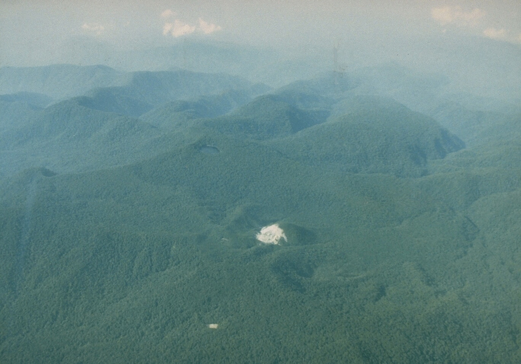 Gunung Patah is a densely forested, eroded Quaternary volcano SE of Dempo volcano. The age of its latest eruptions is not known, although a possible new crater (the light-colored area in the center of this photo) was observed in 1989 about 6 km SE of the summit of Patah volcano. Another crater containing a lake is visible 1 km to the south (bottom-center). Photo by Michael Savill, 1989.