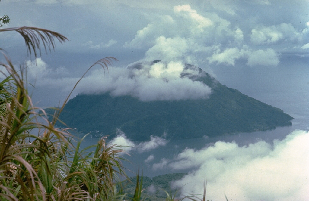 Cloud-capped Hiri volcano forms a small 3-km-wide island, seen here from Gamalama volcano on Ternate Island immediately to the south.  The 630-m-high volcano is mapped as Holocene in age, but has no known historical eruptions. Copyrighted photo by Katia and Maurice Krafft, 1976.