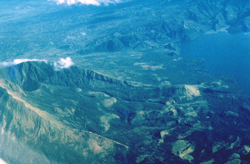 Collapses at the summit or flanks of volcanoes during major volcanic landslides can create large horseshoe-shaped craters that open in the direction of the landslide, like this 2.1 x 3.5 km crater at Iriga in the Philippines. It was produced by a massive landslide during the Holocene. The resulting debris avalanche traveled more than 10 km to the SE and flowed into Lake Buhi at the upper right. This view is from the south, with the summit to the left. Photo by Chris Newhall (U.S. Geological Survey).
