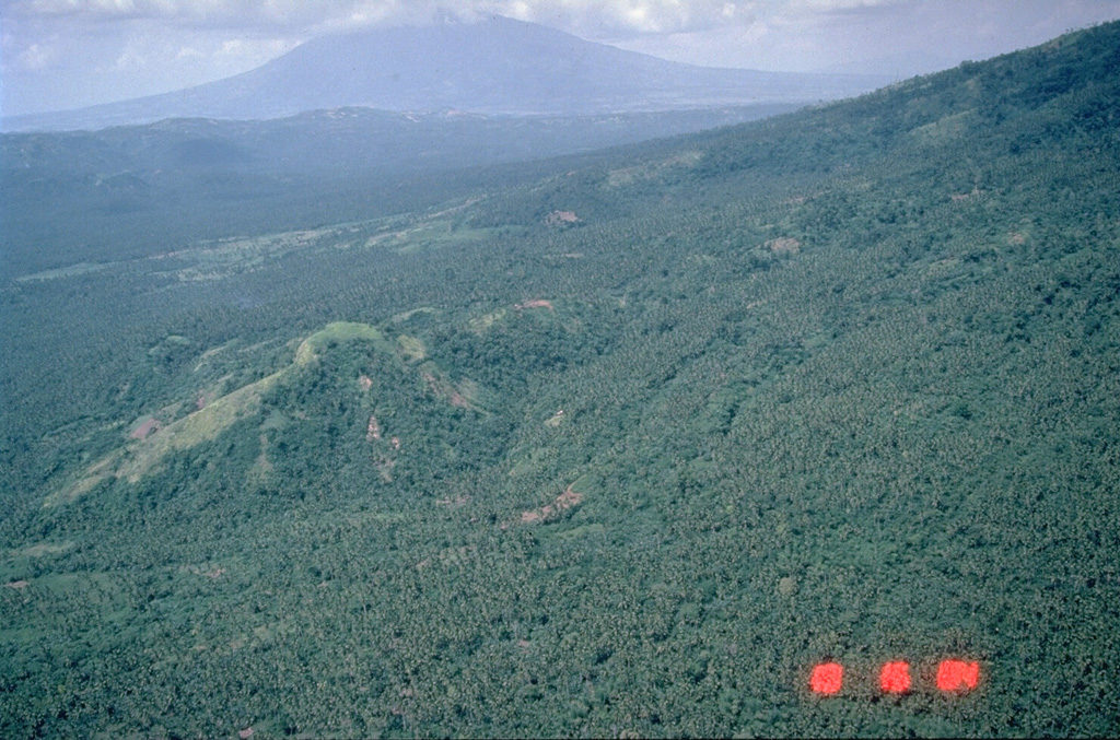 Mount Isarog is seen in the background to the NW beyond the lower flanks of Iriga volcano in the foreground. It occupies the broad isthmus between Lagonoy Gulf and San Miguel Bay. The summit contains a large crater with a  deep and narrow notch on the lower eastern flank. Photo by Chris Newhall (U.S. Geological Survey).
