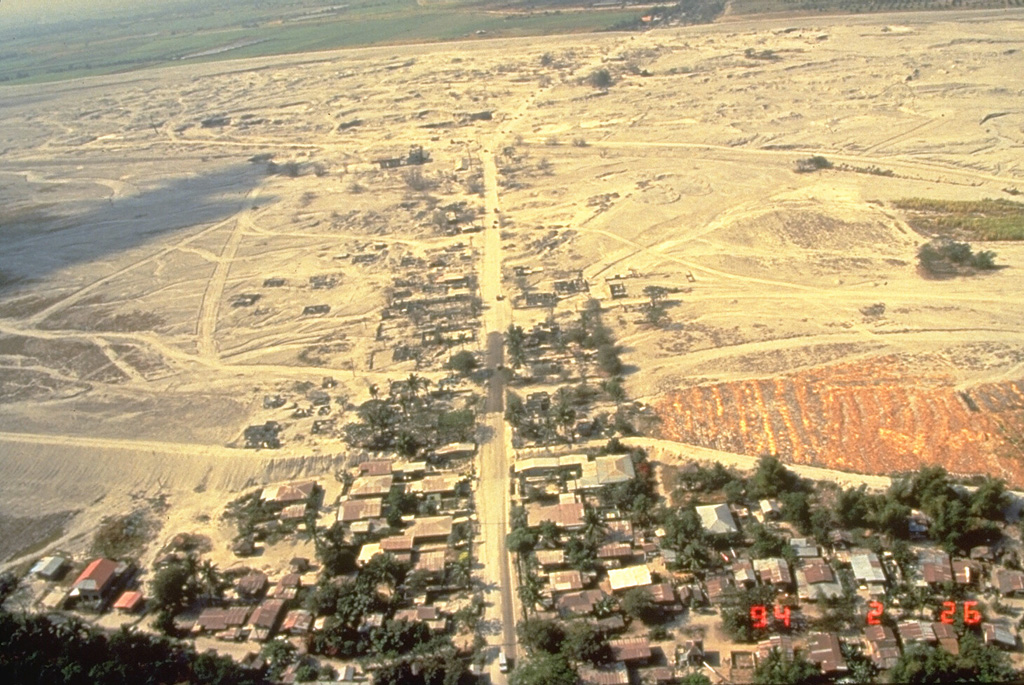 Lahars produced devastating social and economic disruption for many years after the 1991 eruption of Pinatubo in the Philippines. The towns of Barangay Manibaug Pasig in the foreground of this 26 February 1994 view, and Mancatian in the distance, were progressively buried over several years. Construction of lahar levees provided only temporary protection from the massive downstream redistribution of ash and pumice from the 1991 eruption. Photo by Ray Punongbayan, 1994 (Philippine Institute of Volcanology and Seismology).