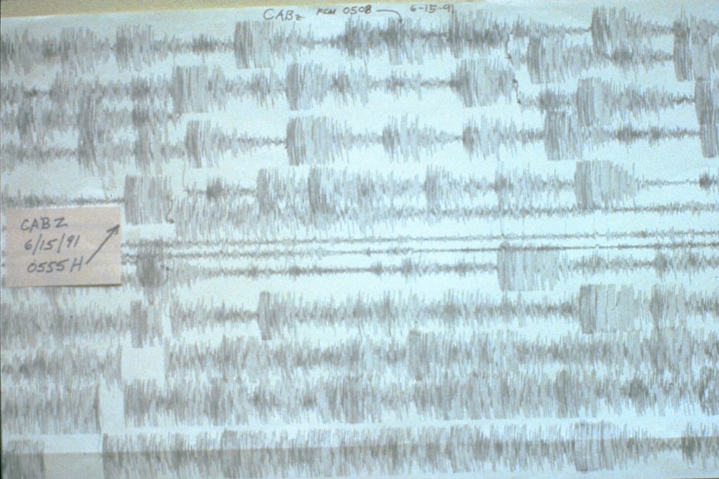 The seismogram for 15 June 1991 shows the intense seismicity accompanying the catastrophic eruption of Mount Pinatubo in the Philippines. This seismic record shows earthquakes over a two-hour period beginning at 0508 hours. The arrow points to the earthquake accompanying a major explosion at 0555, which was preceded by long-period earthquakes. At about 0640 continuous overlapping long-period earthquakes or tremor began, and much of the following record was saturated so that individual earthquakes could not be distinguished.  Photo by Ed Wolfe, 1991 (U.S. Geological Survey).