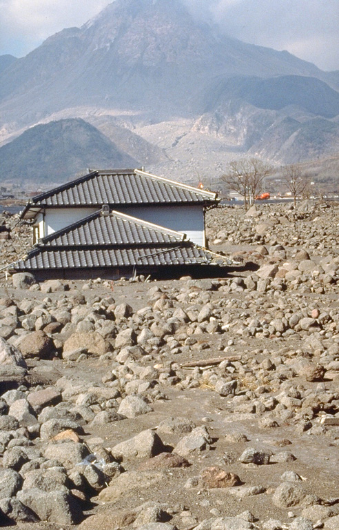 A house on the SW flank of Unzen volcano is buried to its eaves by lahar deposits. Redistribution of material that collapsed from the lava dome (background) produced lahars that devastated populated areas near the volcano. Dome growth, which had begun in May 1991, ceased at about the time of this 3 February 1995 photo. Photo by Tom Pierson, 1995 (U.S. Geological Survey).