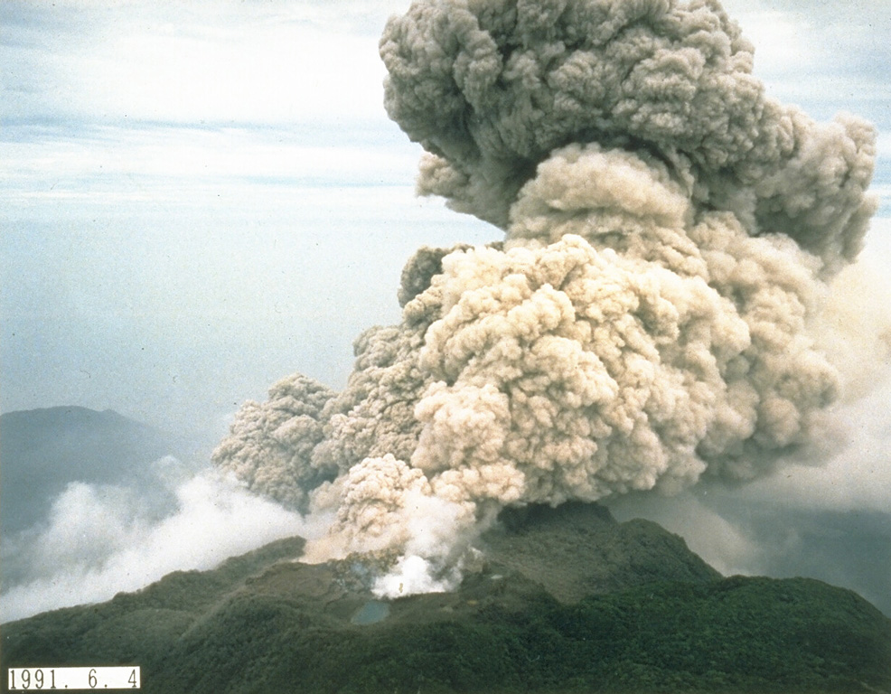 An ash plume rises from the summit crater of Fugendake on 4 June 1991, the day following deadly pyroclastic flows produced by collapse of a portion of the growing lava dome. The small pond in the foreground fills a crater formed by earlier exposions during the eruption that began in November 1990. Photo courtesy Takashi Yamada, 1991 (Public Works Research Institute, Ministry of Construction).