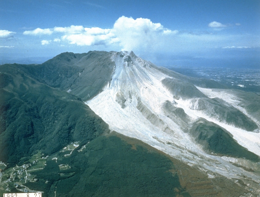 The light-colored area is composed of block-and-ash flow deposits produced by multiple collapse events of the growing lava dome at Unzen. By the time of this 28 August 1992 photo, taken from the SE, pyroclastic flows were traveling down both the Mizunashi valley (center) and the Oshigatani valley (right). Dome growth began in 1991 and continued into 1995. Photo courtesy Takashi Yamada, 1992 (Public Works Research Institute, Ministry of Construction).
