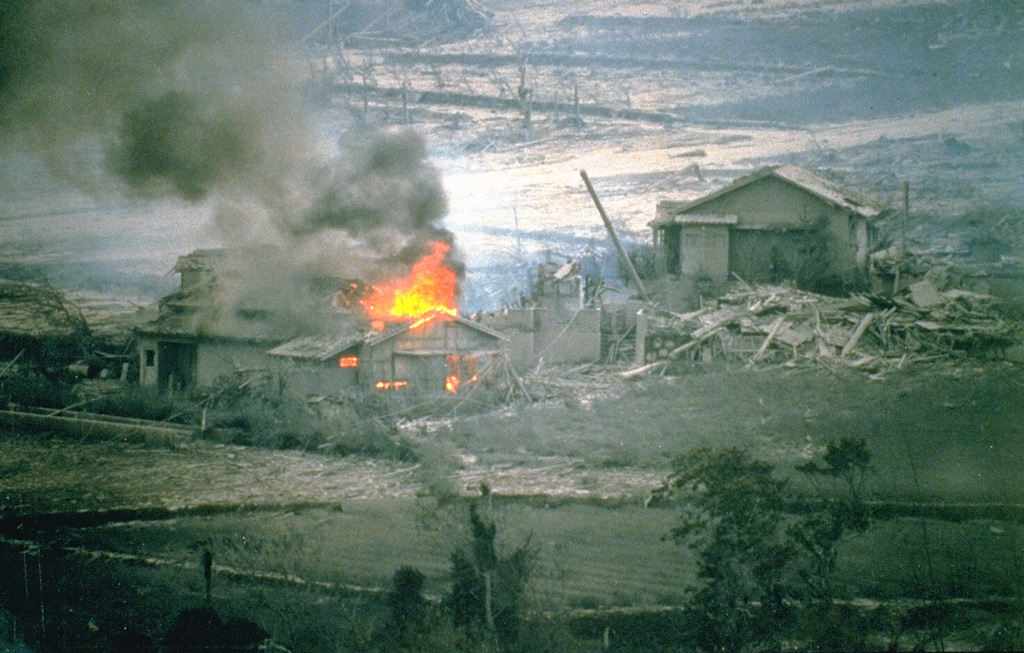 A house that was ignited by a hot block-and-ash flow burns in the Nakao River valley in June 1993. This marked the first destruction of property in drainages NE of Unzen. Pyroclastic flows on 23 June traveled 4 km down the NE flank and resulted in devastation across 1 km of a residential district on the outskirts of Shimabara City. The area had been evacuated since August 1991. One person who had entered the evacuated area to watch their house burn was killed by a second pyroclastic flow. Photo courtesy Takashi Yamada, 1993 (Public Works Research Institute, Ministry of Construction).