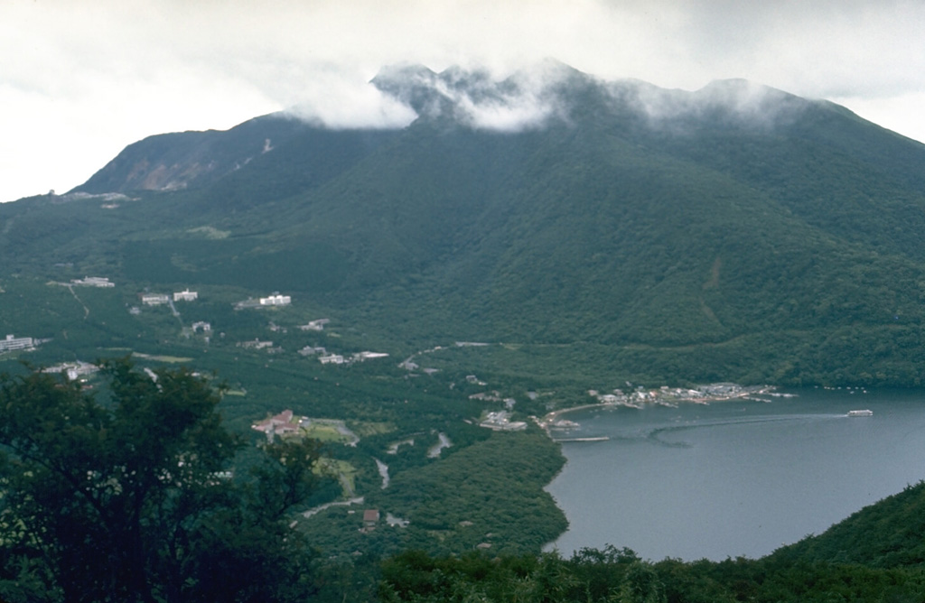 Kamiyama, the highest of a group of lava domes forming the central cone complex of Hakoneyama caldera, rises E of Ashinoko (Lake Ashi). The lake formed about 3,100 years ago when collapse of the NW side of Kamiyama dammed the Hayakawa river valley at the N end of the lake (lower left). Dome growth at Kamiyama occurred about 2,900 years ago. Photo by Lee Siebert, 1977 (Smithsonian Institution).