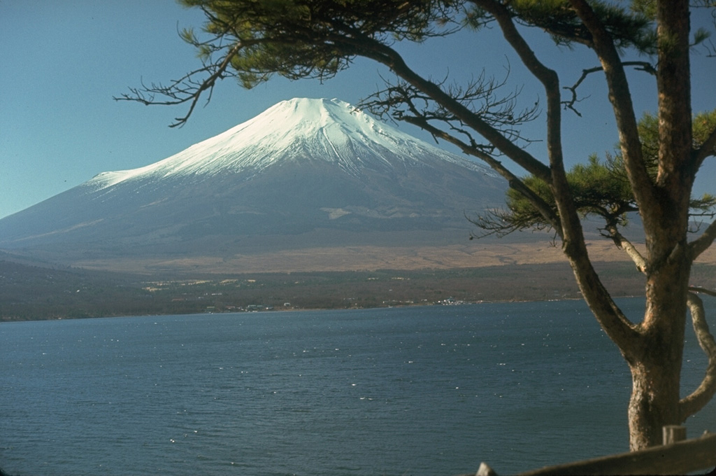 Fuji towers above Lake Yamanaka, one of the Fujigoko (the "Five Lakes of Fuji") that formed when lava flows blocked drainages against a Tertiary mountain range to the N. The smaller ridge at the snowline on the left is Hoeisan, a remant of Kofuji (Old Fuji), one of several older volcanoes above which the modern edifice was constructed. Photo by Lee Siebert, 1970 (Smithsonian Institution).