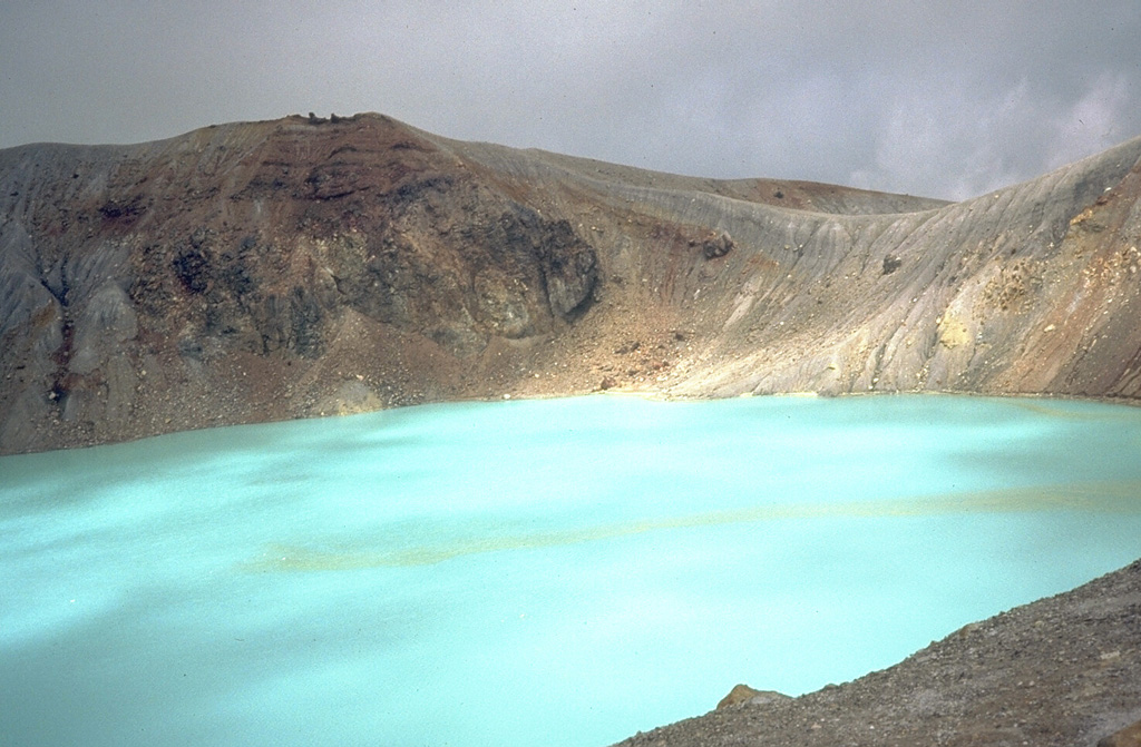 The turquoise waters of Yugama, one of three craters at the summit of Japan's Kusatsu-Shirane volcano, are a popular tourist destination. Yellow rafts of sulfur float on the surface of the acidic lake, which prior to an eruption in 1882, was clear with forested walls. Frequent phreatic explosions have occurred from Yugama and the two other summit craters during historical time. This 1981 photo was taken from the south crater rim. Photo by Dick Stoiber, 1981 (Dartmouth College).