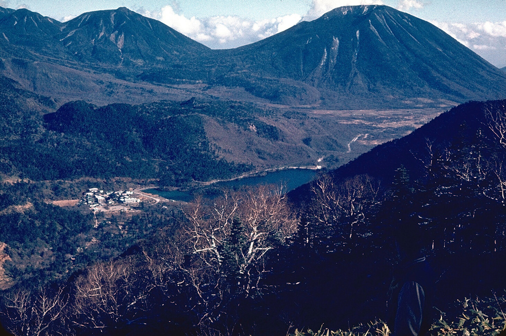 The Omanago volcano group (upper left) consists of a series of five lava domes in Nikko National Park. The highest dome is Omanago, located at the SE end of the complex. Mitsudake is the NW-most dome. The higher northern peak of the Mitsudake complex is out of view to the left, and the lower southern dome forms the low ridge behind the hot spring resort of Yunoko lake in the center of the photo. The peak on the right horizon is Nantaisan. Photo by Lee Siebert, 1964 (Smithsonian Institution).