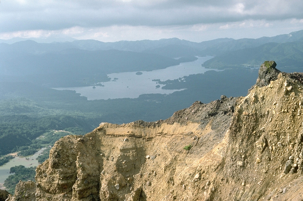Lake Hibara in the distance was created in 1888 when the partial collapse of Ko-Bandai volcano produced a large debris avalanche that traveled 11 km, nearly to the far end of the lake. The area in front of the lake and the islands in the lake are part of the debris avalanche deposit. The steep wall in the foreground is part of the back headwall of the avalanche scarp. Photo by Lee Siebert, 1988 (Smithsonian Institution).