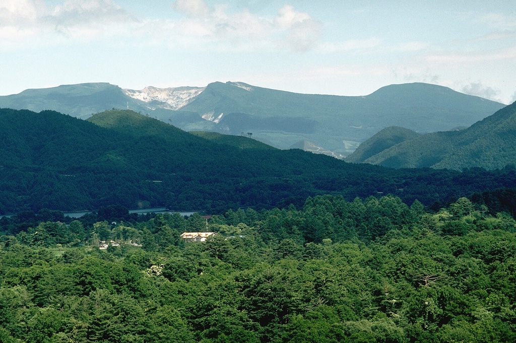 The broad Adatara massif is composed of a group of cones and lava domes, seen here from the W. The unvegetated area on the left summit ridge is a 1-km-wide circular crater that has been mined for sulfur. Seventy-two miners working in the crater were killed during an explosive eruption in 1900. Photo by Lee Siebert, 1988 (Smithsonian Institution).