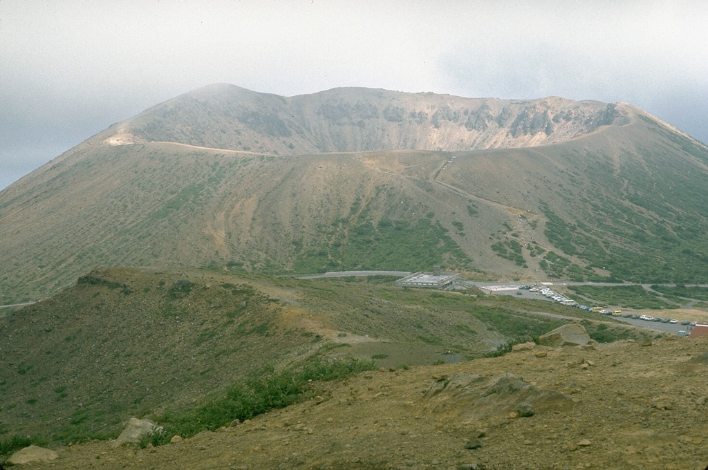 The Azuma Kofuji cone with its 300-m-wide crater is one of many volcanic features of the Azumayama complex. This volcano group consists of a cluster of cones and lava domes. Volcanic activity has migrated to the E, with the Higashi-Azuma volcano group being the youngest. This photo was taken from the NW on the flanks of Issaikyoyama, which has been the site of historical eruptions (mostly small phreatic explosions). Photo by Lee Siebert, 1988 (Smithsonian Institution).