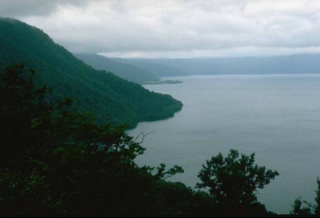 The 11-km-wide lake-filled Towada caldera formed during as many as six major explosive eruptions over a 40,000-year period ending about 13,000 years ago. This view from the south shows the western and northern caldera rims, which reach up to 500 m above the lake. The base of the caldera is 380 m below the lake surface.  Photo by Lee Siebert, 1977 (Smithsonian Institution).