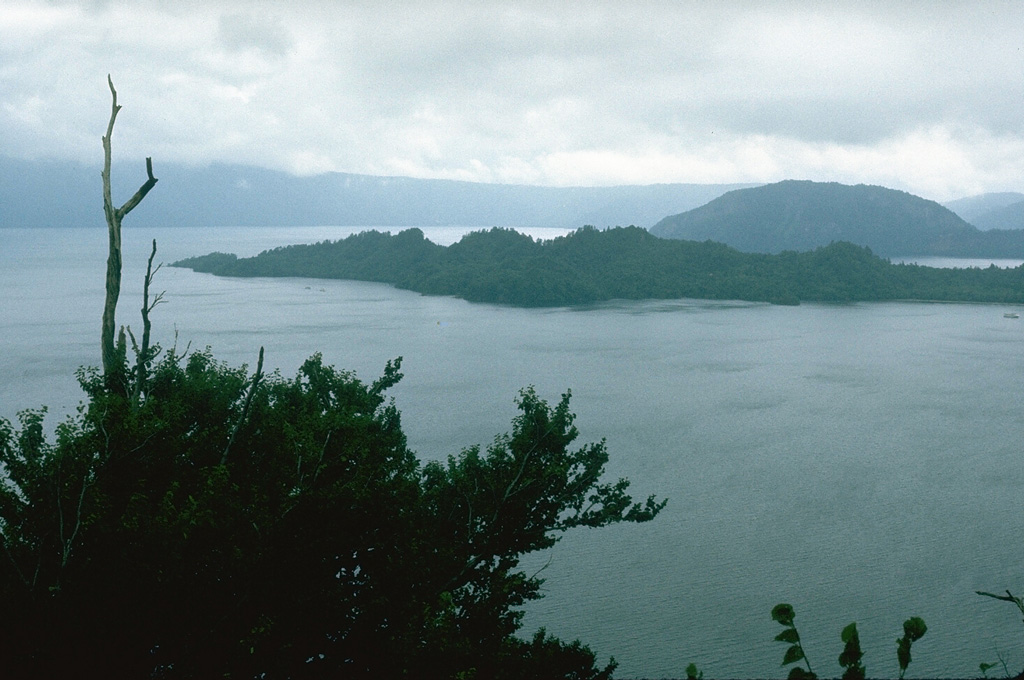 The rounded Ogurayama lava dome to the upper right formed at the end of the 915 CE Towada eruption. Three eruptions were accompanied by the emplacement of the 5 km3 Kemanai pyroclastic flow, which covered several large wooden buildings along the Yonesawa River. The dome formed along the NE rim of the Nakanoumi caldera, with its SW rim forming the peninsula in the center of the photo. The northern wall of Towada caldera appears in the distance. Photo by Lee Siebert, 1977 (Smithsonian Institution).