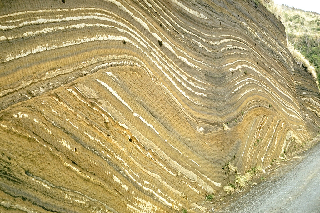 This outcrop at Oshima volcano, in the Izu Islands south of Tokyo, shows more than 100 individual tephra layers. They were produced by eruptions of Oshima at fairly regular intervals over a period of about 10,000 years. The lower layers follow the older preexisting topography. A prominent unconformity in the center of the outcrop is an erosional surface that truncated the earlier eruption deposits. The upper layers mantled this uneven surface. Photo by Richard Fiske, 1961 (Smithsonian Institution).
