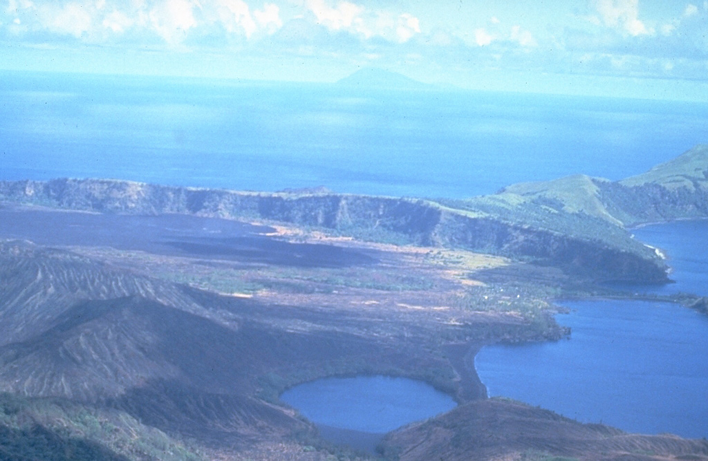 This south-looking view across Pagan Island shows Alamagan Island in the distance. The wall across the center of the photo is the southern rim of a 7-km-wide caldera containing North Pagan volcano. The lake in the foreground is the westernmost of two maars on the western flank of North Pagan. The black lava flow on the caldera floor at the left center in this 16 June 1981 photo erupted from a vent on the south rim beginning on 15 May 1981. Photo by U.S. Navy, 1981.