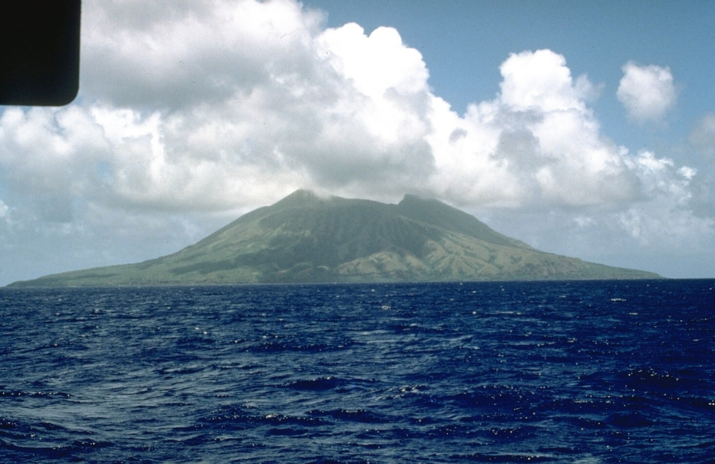 Alamagan, seen here from the W with two peaks on either side of a roughly 350-m-deep summit crater, is the emergent summit of a large submarine volcano. The exposed cone is largely Holocene in age and the SW flank contains a 1 x 1.6 km graben. Pyroclastic flow deposits have been dated at about 1,000 years old. Photo by Norm Banks, 1981 (U.S. Geological Survey).