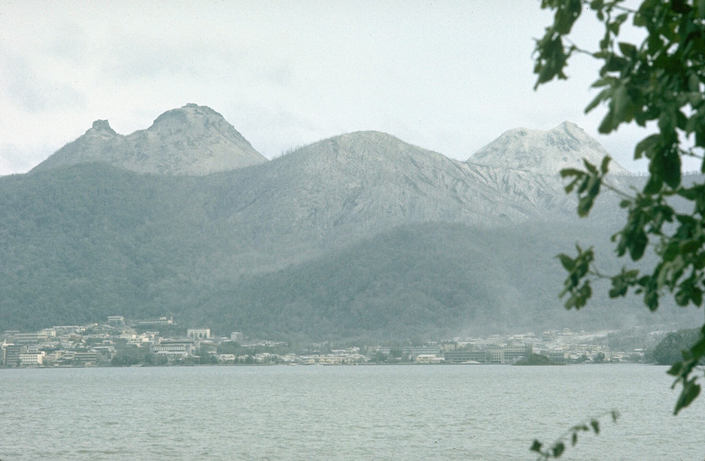 Usu rises to the SE above the town of Toyako Spa on the shores of Lake Toya on 12 August 1977. O-Usu (left) and Ko-Usu (right) lava domes are within the summit caldera. The first of three major explosive eruptions during 7-9 August originated from vents behind Ko-Usu in this view and stripped trees of vegetation on the upper slopes. Growth of a new lava dome in the area between the two domes later in the eruption greatly changed the morphology of the summit. Photo by Lee Siebert, 1977 (Smithsonian Institution).