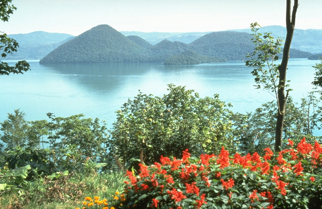 A group of lava domes form Nakanojima, an island in the center of Lake Toya. The lake fills the 10-km-wide caldera, which formed following a major explosive eruption about 110,000 years ago. The photo was taken from the flank of Usu volcano on the southern rim of the caldera. Photo by Norm Banks, 1981 (U.S. Geological Survey).