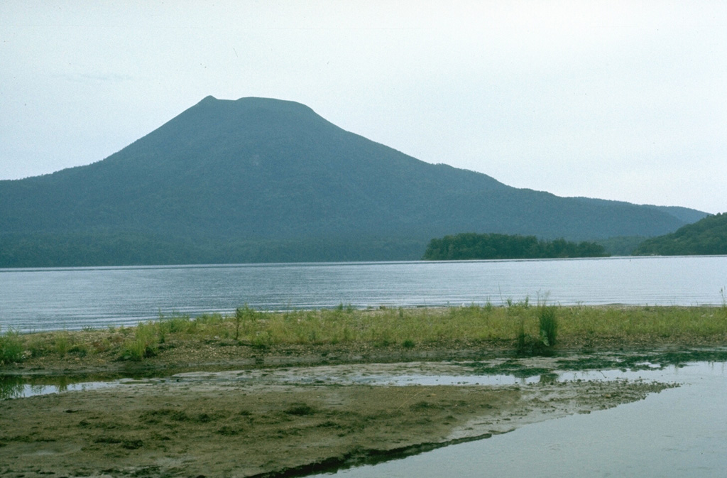 Oakandake, the largest post-caldera cone at Akan volcano, is seen here from the W across the Akan Caldera lake. It was constructed at the NE end of the 13 x 24 km caldera, opposite a cluster of stratovolcanoes at the SW end. Meakan in the SW group has been frequently active. Photo by Lee Siebert, 1977 (Smithsonian Institution).