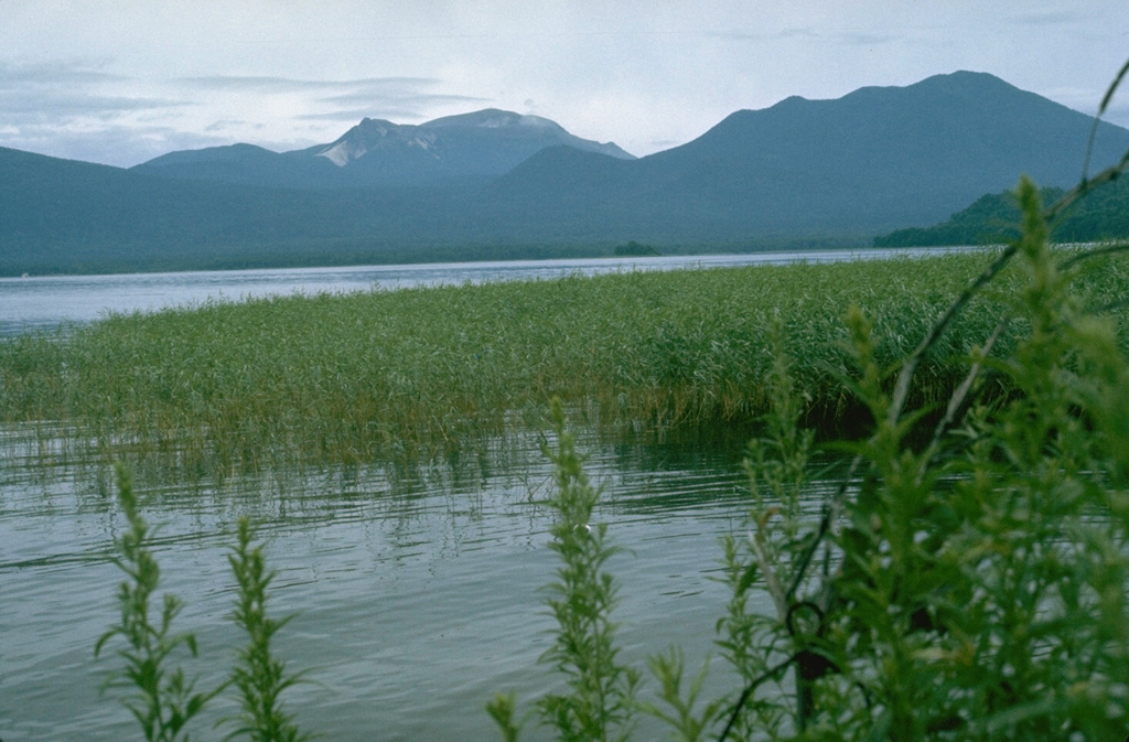 Meakan volcano (left center) rises above Lake Akan to its NE. Along with Fuppushi volcano (right), it is part of a cluster of nine cones within the SW side of the 13 x 24 km Akan Caldera. The summit of Meakan contains the active Ponmachineshiri and Nakamachineshiri craters, which have been the sites of frequent phreatic eruptions in historical time.  Photo by Lee Siebert, 1977 (Smithsonian Institution).