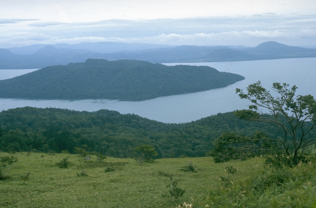 The 20 x 26 km Kussharo caldera, seen here from its western rim, is the largest of a cluster of calderas in NE Hokkaido. It formed around 30,000 years ago. Nakajima, a Holocene post-caldera lava dome complex, forms the large island to the left that fills much of the western half of the caldera. Atosanupuri is located near the center of the caldera, east of the lake.  Photo by Lee Siebert, 1977 (Smithsonian Institution).