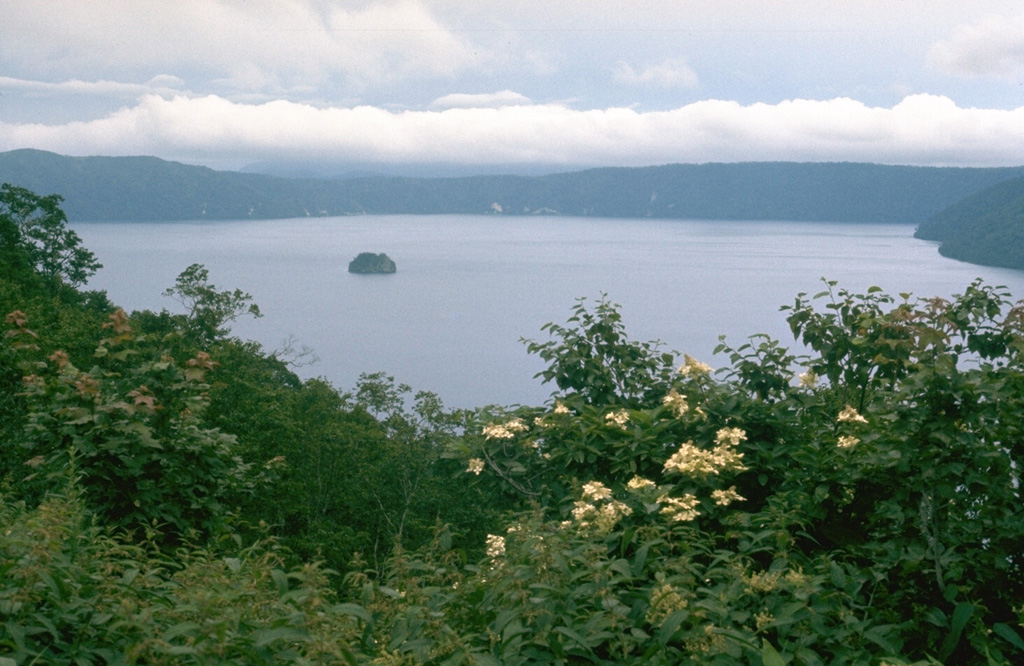 Mashu is a 6-km-wide caldera on the northernmost Japanese island of Hokkaido, seen here from the SW rim with the Kamuishi Island lava dome in the center of the lake. It truncates a stratovolcano on the ESE rim of the larger Kutcharo caldera. The latest eruption of Mashu took place about 1,000 years from Kamuinupuri, the lower flanks of which appear to the far-right.  Photo by Lee Siebert, 1977 (Smithsonian Institution).