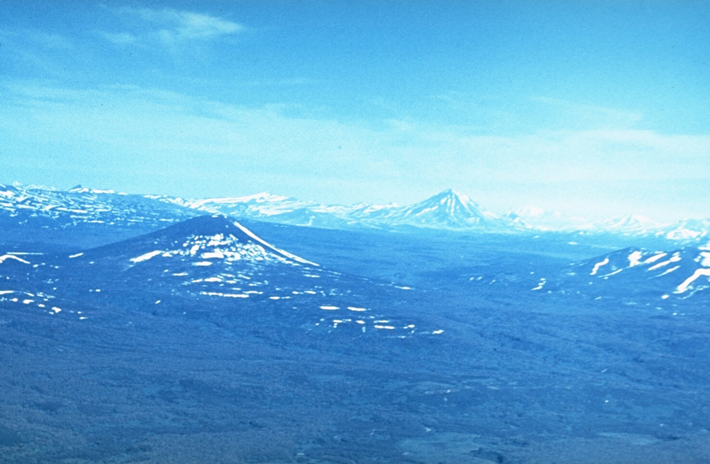 Visokiy (left of center) is surrounded by young lava flows produced by regional basaltic volcanism, seen here from the southwest. Mutnovsky is the cone on the horizon and to the left is Gorely. Photo by Andrei Tsvetkov, 1977.