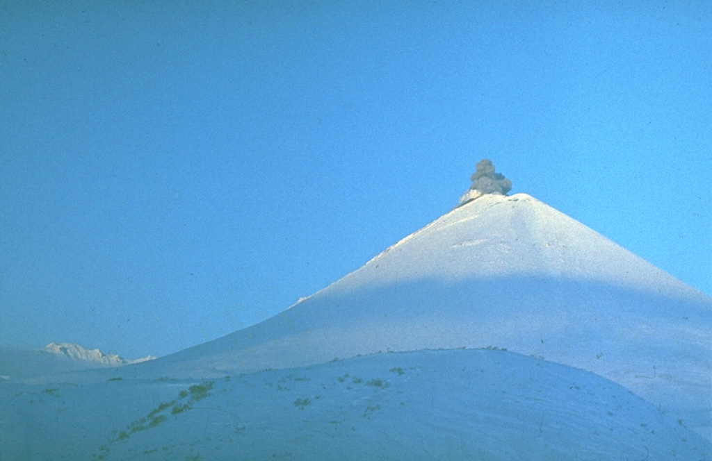 A small ash plume rises from the summit crater of Karymsky in this photo taken during the 1970's. Near-continuous mild-to-moderate explosive eruptions took place during 1970-82. Lava flows were emitted from the summit crater in 1970, 1971, 1976, and 1979-82. Photo by Yuri Doubik (Institute of Volcanology, Petropavlovsk).