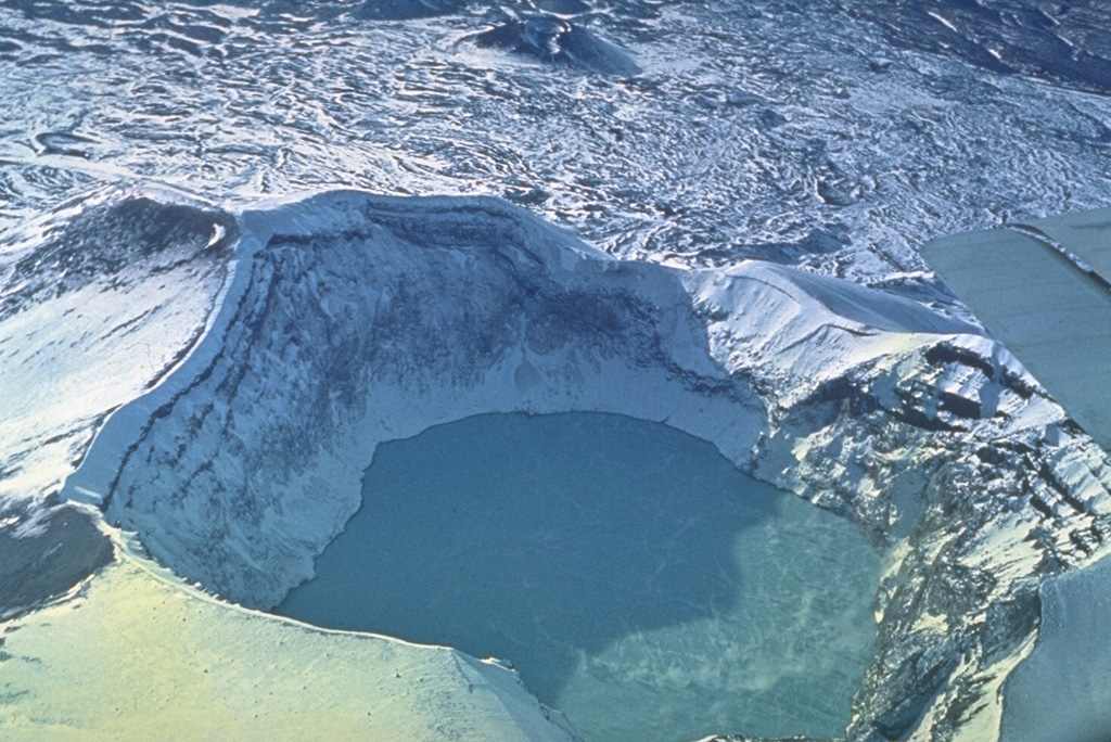 A crater lake fills Troitsky crater, the youngest of six craters capping the elongated summit of Maly Semiachik volcano in central Kamchatka. Steam rises from the surface of the hot, acidic crater lake in this early 1970s photo. The lake has a maximum depth of about 140 m. Temperatures as high as 41°C have been recorded, along with pH levels down to 0.4. Photo by Oleg Volynets (Institute of Volcanology, Petropavlovsk).