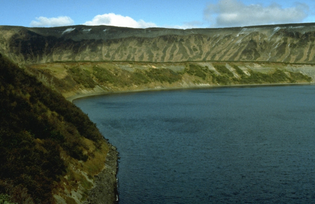 The Lake Dalny maar formed about 7,600-7,700 years ago in the the northern area of Uzon caldera. Tephra deposits from this eruption are found within 5 km from the lake. The 1-km-wide maar is surrounded by a 60-m-high tephra ring that forms the flat slope on the far side of the lake. The northern wall of Uzon caldera rises behind it. Photo by Dan Miller, 1990 (U.S. Geological Survey).