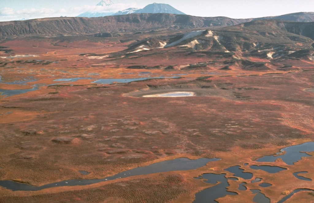 The Uzon and Geyzernaya calderas, containing Kamchatka's largest geothermal area, form a 7 x 18 km depression that formed during the mid-Pleistocene. Post-caldera activity was largely Pleistocene in age, although the Lake Dal'ny maar formed during the early Holocene. This view looks from the SW across the flat caldera floor, which contains numerous lakes, streams, and thermal areas. Sharp-peaked Kronotsky volcano and flat-topped Krasheninnikov volcano appear in the distance beyond the N caldera rim. Photo by Dan Miller, 1990 (U.S. Geological Survey).