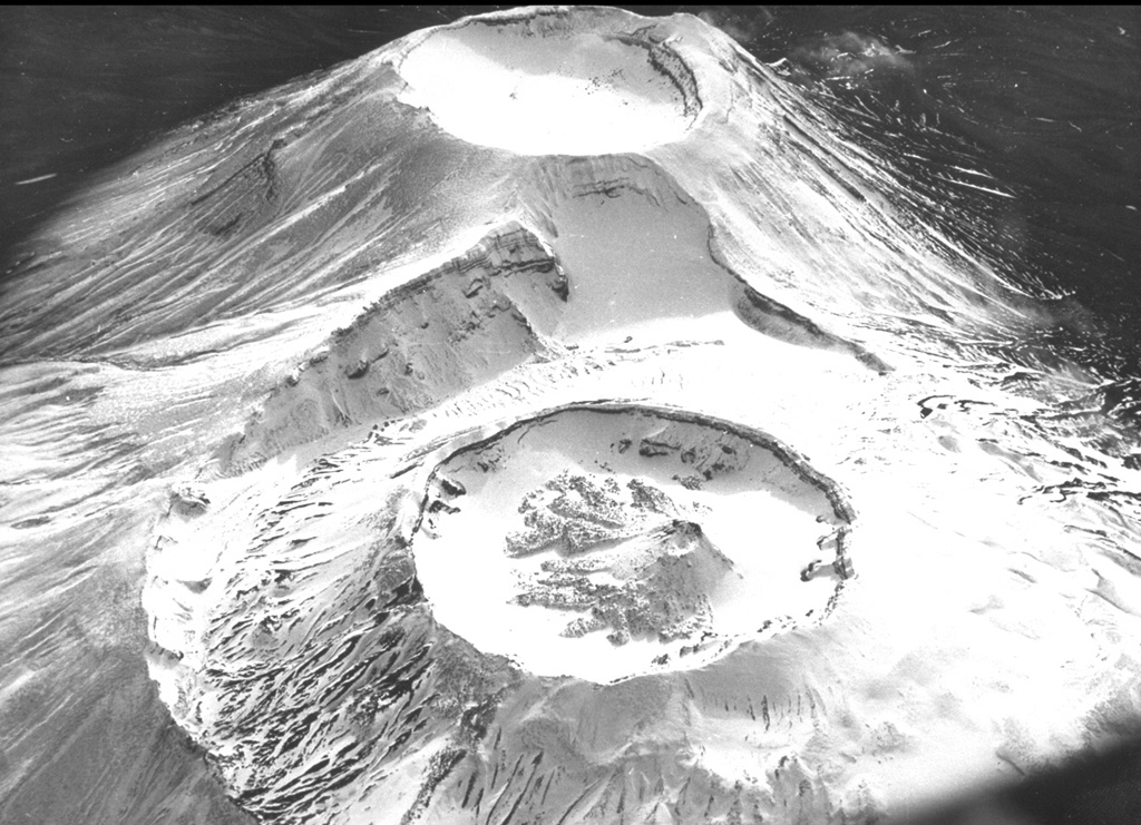 Krasheninnikov is comprised of two overlapping edifices seen here from the north, with both cones topped by 800-m-wide craters. Construction of the northern cone (bottom) began about 6,500 years ago and eventually formed an inner cone within a 2-km-wide crater, the rim of which is visible to the left. The small inner cone of the northern crater was built during an eruption about 400 years ago which also produced a SW-flank lava flow. Photo courtesy of Anatoli Khrenov, 1989 (Institute of Volcanology, Petropavlovsk).