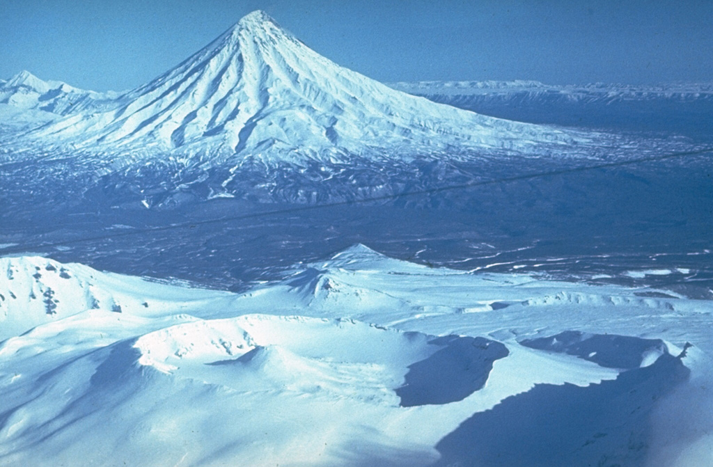 Kronotsky is seen here to the NE of the broad summit of Krasheninnikov in the foreground. The slopes of the largely Pleistocene Kronotsky contain deep erosional valleys and had weak phreatic eruptions during the 20th century. Krasheninnikov has been active throughout the Holocene.  Photo by Yuri Doubik (Institute of Volcanology, Petropavlovsk).