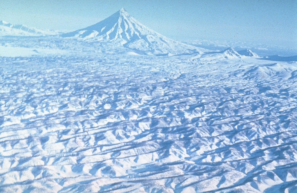 Kronotsky, seen here from the SW, towers above extensively eroded pyroclastic flow deposits. These voluminous deposits were produced by Pleistocene explosive eruptions that resulted in formation of the Uzon and Krasheninnikov calderas. The initial caldera-forming eruption at Uzon dates back to the mid-Pleistocene. A younger caldera formed about 39,000 years ago and was followed shortly by formation of the Krasheninnikov caldera. Photo by Yuri Doubik (Institute of Volcanology, Petropavlovsk).