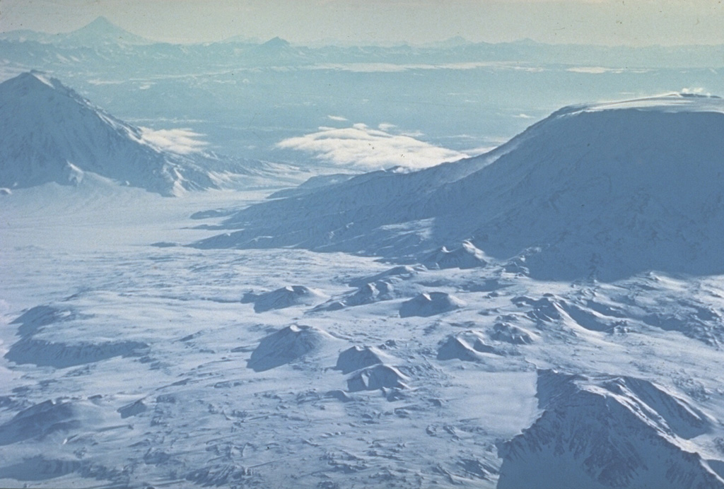 The summit of flat-topped Plosky Tolbachik volcano (right) contains a 3-km-wide, glacier-filled caldera. Scoria cones line a rift zone that extends to the NE. Another rift zone that extends 70 km SSW of the summit has been the site of frequent basaltic eruptions during the Holocene, including the "Great Tolbachik Fissure Eruption" of 1975-76. Udina rises to the left, with Kronotsky on the far horizon to the SSE. Photo by Oleg Volynets (Institute of Volcanology, Petropavlovsk).