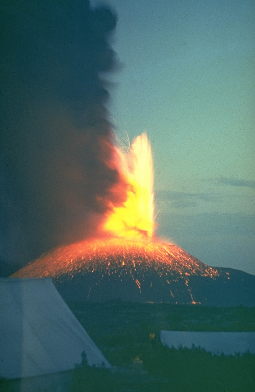 A lava fountain and ash plume rise above a volcanological field camp on Tolbachik volcano in July 1975. This photo was taken several days after the onset of activity along the southern rift zone on 6 July, and by this time the new scoria cone had grown to a height of 200 m. The upper flanks of the cone are blanketed by incandescent volcanic bombs. Photo by Yuri Doubik, 1975 (Institute of Volcanology, Petropavlovsk).