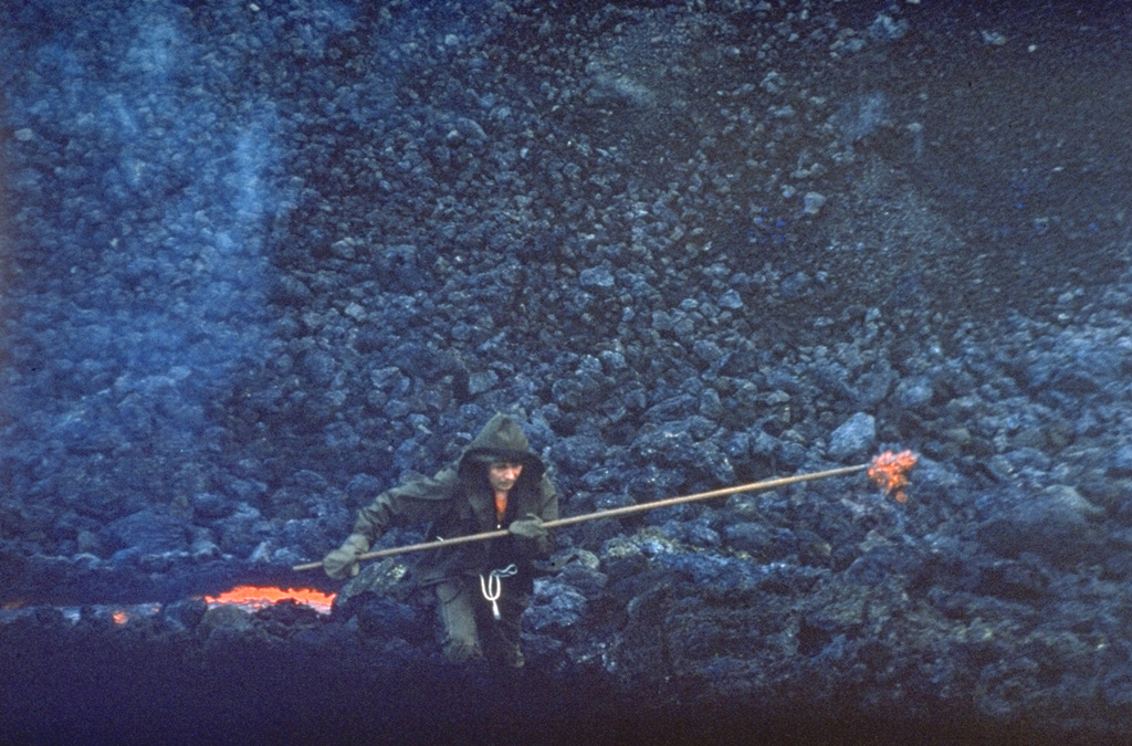 A scientist gathers a sample of molten lava from a vent at the base of a new scoria cone in April 1976. Scientists from the Institute of Volcanology in Petropavlovsk analyzed lava samples throughout the eruption to determine the geochemical variation of eruptive products. The basaltic flow was one of several emplaced during a major SSW-flank eruption of Tolbachik in 1975-76. Photo by Oleg Volynets, 1976 (Institute of Volcanology, Petropavlovsk).